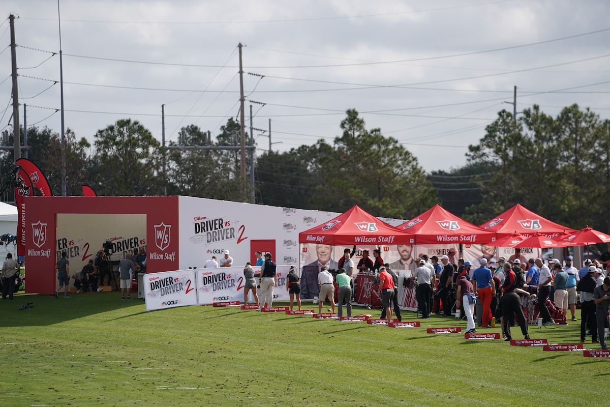 People gathered outside a product demo booth and trying out golf clubs