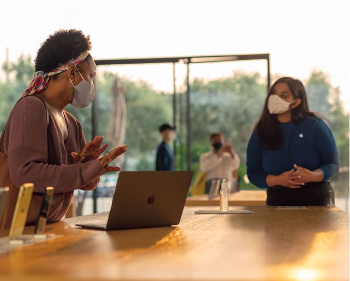 Customer talking to a Genius Bar rep while standing in front of iPhones and a computer