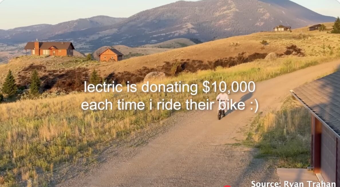 Scenic rural landscape with golden hills and mountains in the background, featuring a dirt road winding through grassland. White text overlay reads "lectric is donating $10,000 each time i ride their bike :)" with "Source: Ryan Trahan" credited at bottom right.