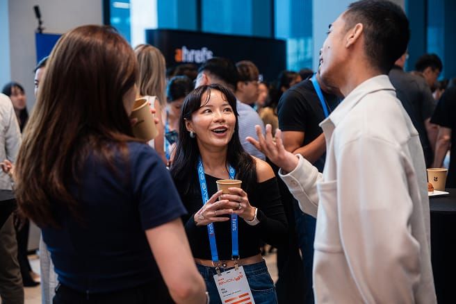 Three people in conversation at a conference, one woman looking up and smiling.