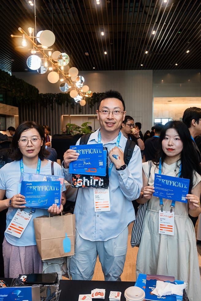 Three people, two women and one man, standing and holding up bright blue certificates and gift bags at a conference.
